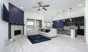 Relax in a spacious living area with a comfortable sofa set and fireplace. Enjoy a well-equipped kitchen with a sleek island and large windows offering views of the surrounding area.