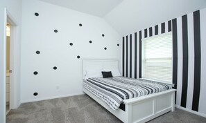 Cozy retreat with a patterned bedspread and striped walls, featuring a comfortable bed and stylish decor.