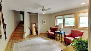 A spacious living room with a wooden staircase, a ceiling fan, and a large window with blinds. - Johnny Appleseed by Taylor Made Deep Creek (Oakland)