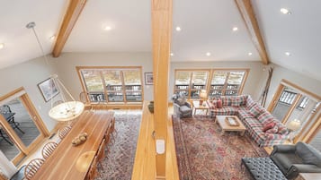 A spacious loft with a high ceiling, large windows, a wooden dining table, a sofa, and a fireplace.