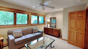 A living room with a sofa, glass coffee table, wooden cabinet, and a door. - Johnny Appleseed by Taylor Made Deep Creek (Oakland)
