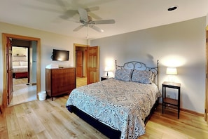 Quarto com cama, ventilador de teto, televisão e cômoda.