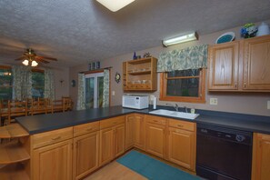 A kitchen with wooden cabinets, a dishwasher, a microwave, and a dining area with chairs and a table. - Just About Paradise by Taylor Made Deep Creek (Oakland)