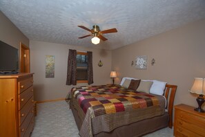 A bedroom with a wooden dresser, a bed with a quilt, a ceiling fan, and a window with curtains. - Just About Paradise by Taylor Made Deep Creek (Oakland)