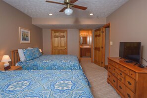 A bedroom with two beds, a ceiling fan, a dresser, and a television.