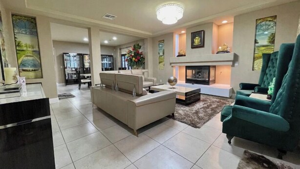 A spacious living room with a fireplace, a sofa, and a green armchair. There is a dining area in the background and a kitchen visible through an open door. - Luxury, Cheerful & Spacious 5 Bedroom Home! Free P (Las Vegas)