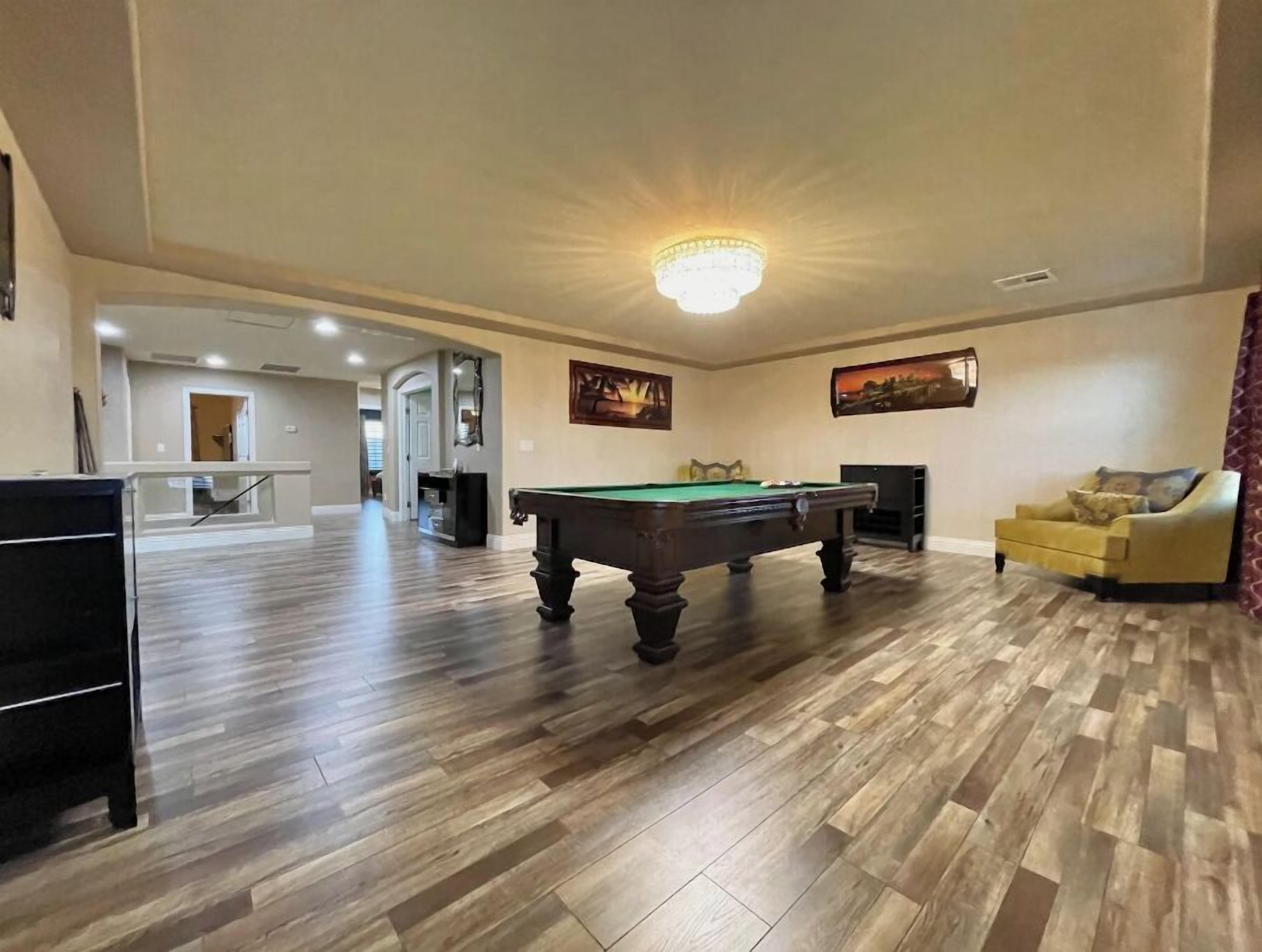 A spacious living room with a pool table, a yellow armchair, and a chandelier.