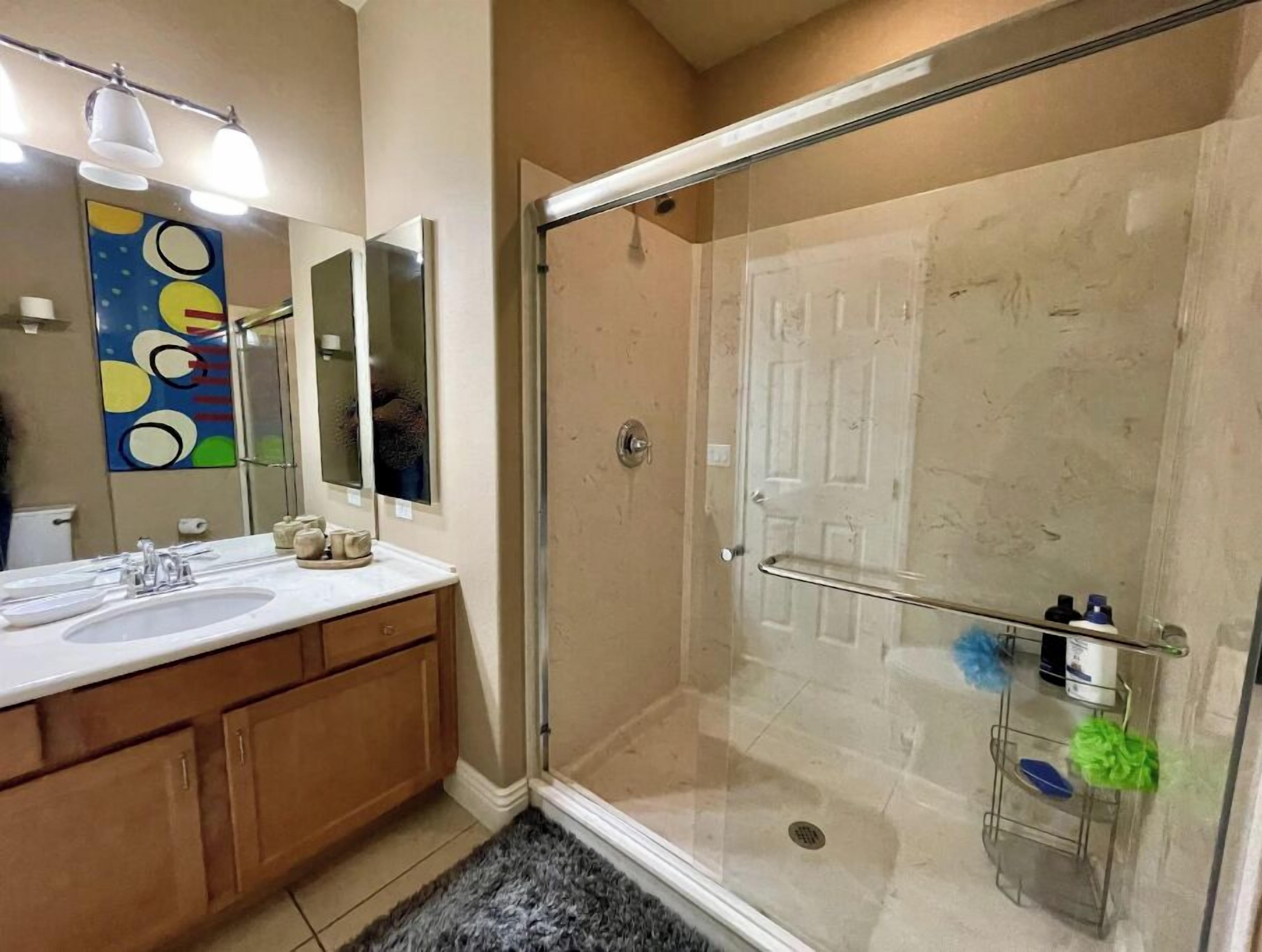 A modern bathroom with a glass shower enclosure, a large mirror, and a sink with a vanity.