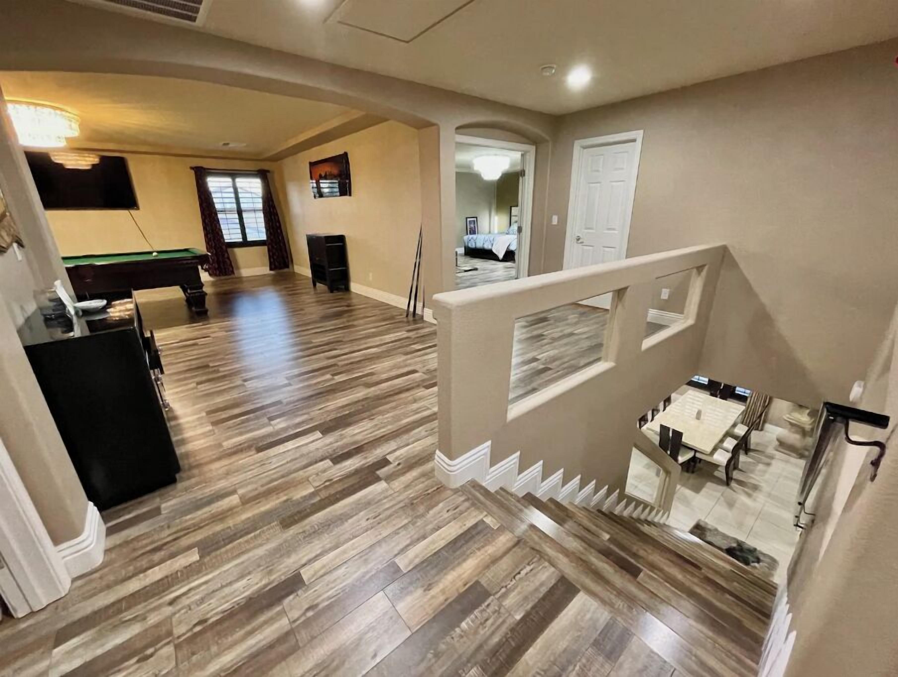 Un amplio espacio de sala con mesa de billar, una escalera y vistas a otra habitación.