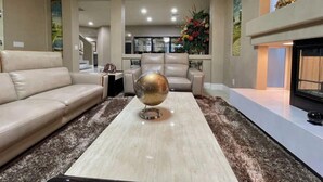 A modern living room with a beige sofa, a coffee table with a decorative globe, a fireplace, and a view into the kitchen area. - Luxury, Cheerful & Spacious 5 Bedroom Home! Free P (Las Vegas)