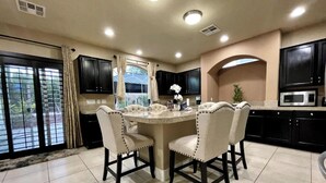 A kitchen with a central island, four chairs, dark cabinets, a microwave, and a window with curtains. - Luxury, Cheerful & Spacious 5 Bedroom Home! Free P (Las Vegas)