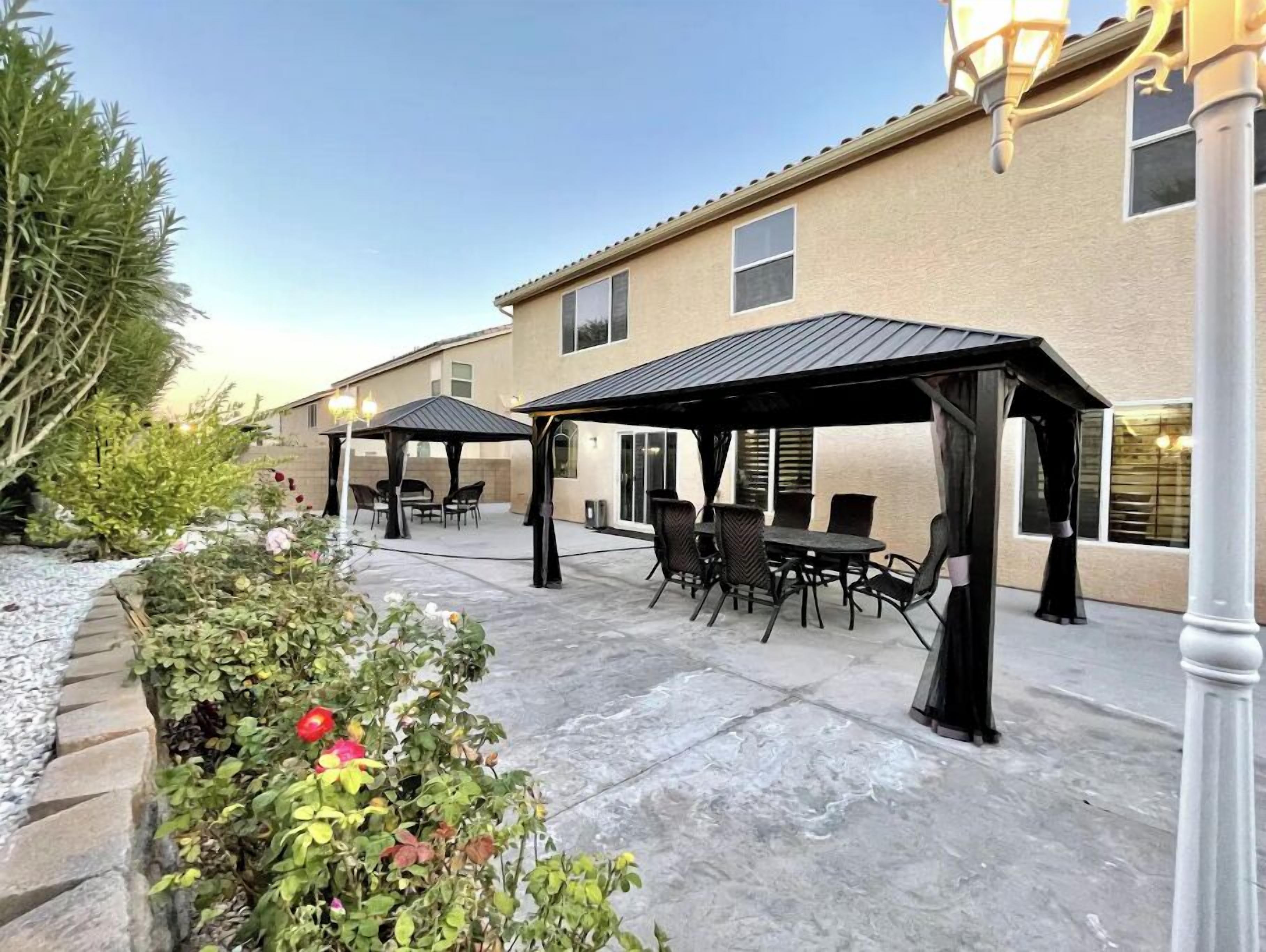 An outdoor patio area with two covered seating areas, a stone pathway, and a building with a beige exterior.