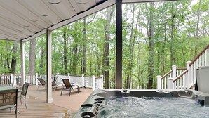 Een hottub op een houten terras met uitzicht op een bos.