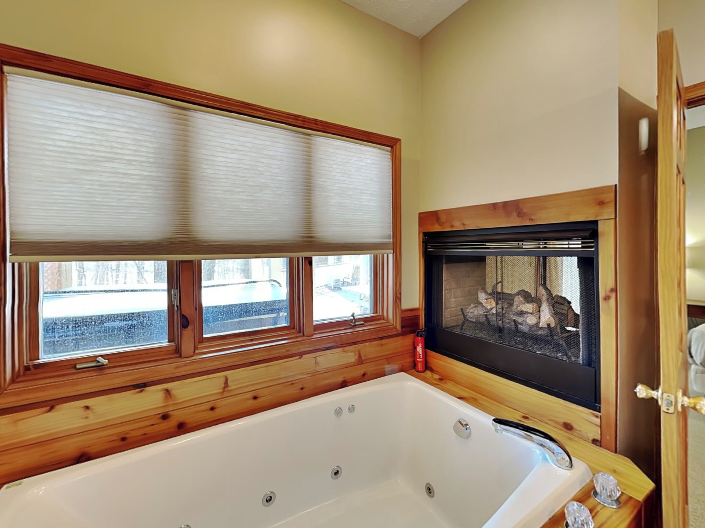 A bathroom with a wooden bathtub, a fireplace, and a window with blinds.