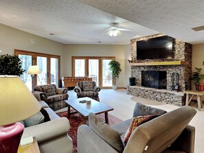 A spacious living room with a stone fireplace, comfortable seating, and large windows. - Lake Dreaming by Taylor Made Deep Creek (McHenry)