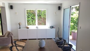 Un comedor moderno con una mesa de madera y sillas negras, un armario blanco con espejo, y vistas a la vegetación por la ventana.