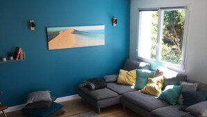 Una sala de estar moderna con una pared azul de acento, un sofá modular con muchos cojines, una mesa de centro de vidrio y un gran ventanal que proporciona luz natural.