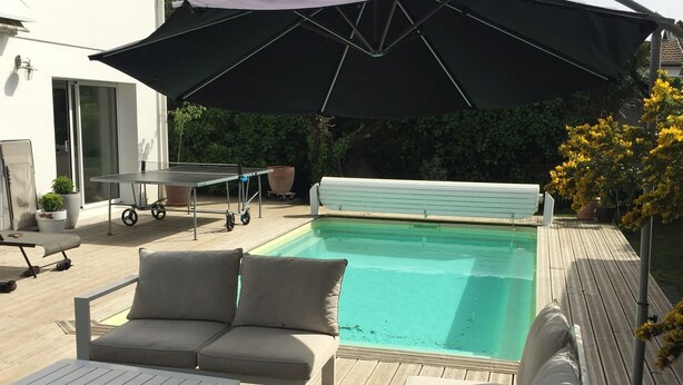 Una zona junto a la piscina con un espacio de estar cubierto, una mesa y una tumbona.