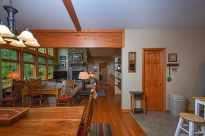 A spacious living room with a fireplace, wooden furniture, and large windows offering a view of the outdoors. - Lake House by Taylor Made Deep Creek (Oakland)