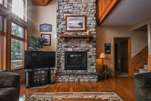 A living room with a stone fireplace, a flat-screen TV, and a staircase.