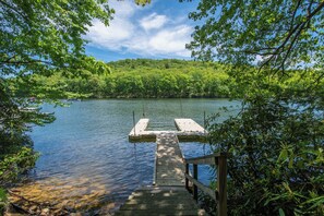 A wooden dock extending into a calm lake surrounded by dense greenery. - Lake Life HQ by Taylor Made Deep Creek (McHenry)