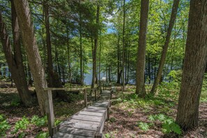 A wooden boardwalk leading through a forested area with a lake in the background. - Lake Life HQ by Taylor Made Deep Creek (McHenry)