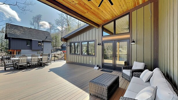 Una terraza techada al aire libre con ventilador de techo, mobiliario de mimbre y vista a una casa en el fondo.