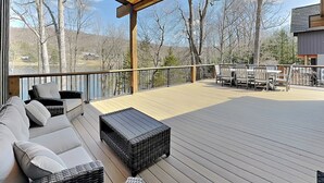 Una terraza techada con mobiliario exterior, vista a árboles y un paisaje lejano.