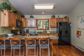 A kitchen with wooden cabinets, a black refrigerator, a granite countertop, and a window with a view of trees. - Lake Reflections by Taylor Made Deep Creek (McHenry)