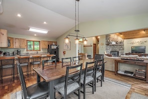 A spacious kitchen with wooden cabinets, a large island, and a dining area with chairs. - Lake Reflections by Taylor Made Deep Creek (McHenry)