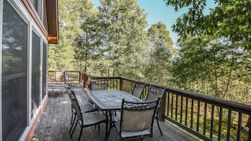 A wooden deck with a table and chairs, overlooking a forested area.