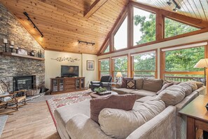 A spacious living room with a stone fireplace, a large window, and a cozy seating area. - Lake Reflections by Taylor Made Deep Creek (McHenry)