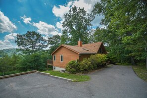 A single-story wooden cabin with a chimney, surrounded by lush greenery and trees. - Lake Reflections by Taylor Made Deep Creek (McHenry)