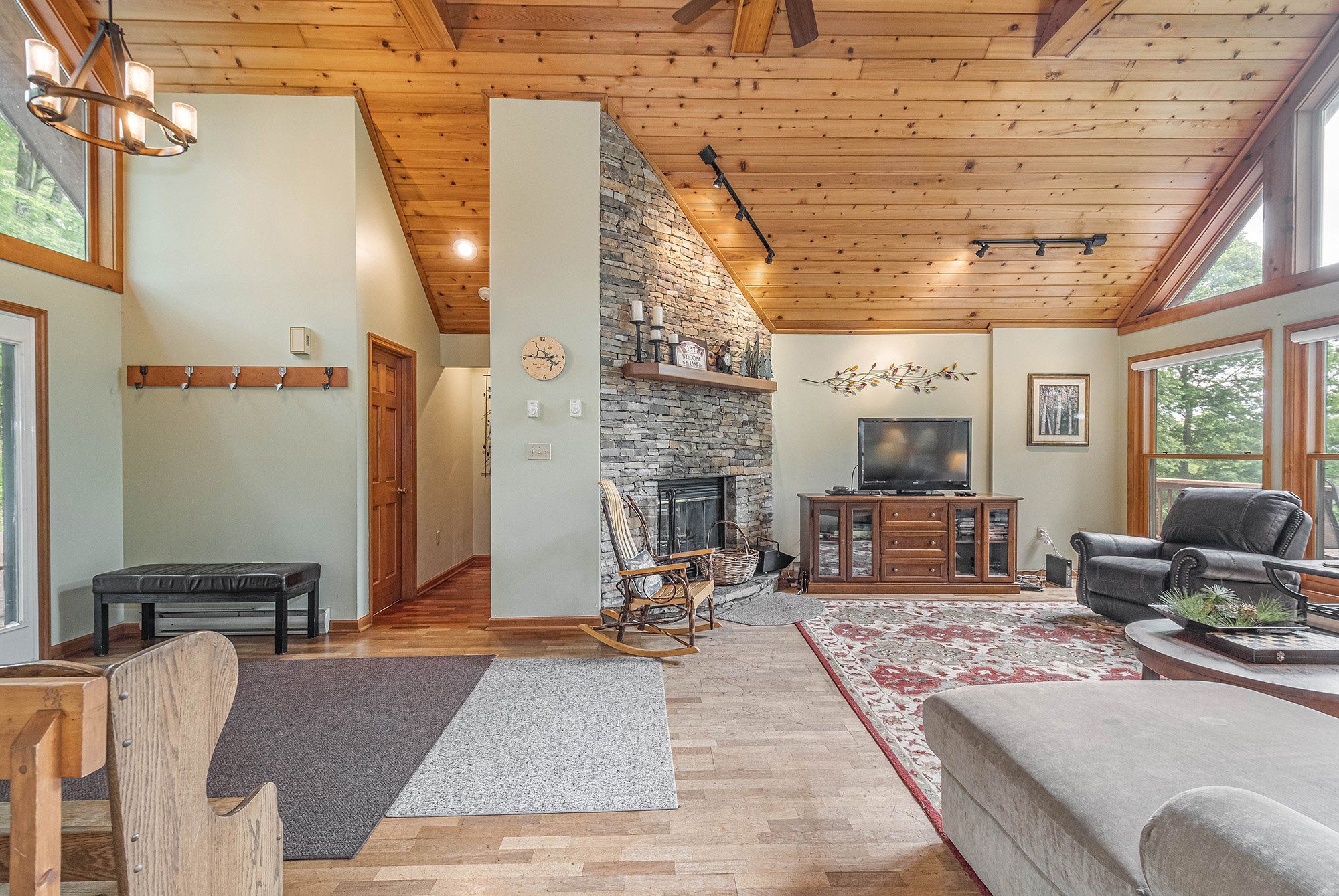 A cozy living room with a stone fireplace, wooden ceiling, and a large window.