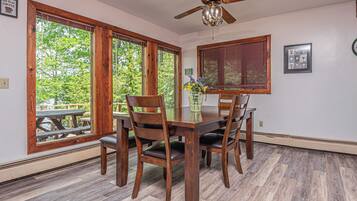 A dining area with a wooden table and chairs, large windows with wooden frames, and a ceiling fan.