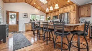 A spacious kitchen with wooden cabinets, a central island with bar stools, and a large refrigerator.
