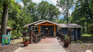 A wooden deck leading to a house with a porch, surrounded by trees.