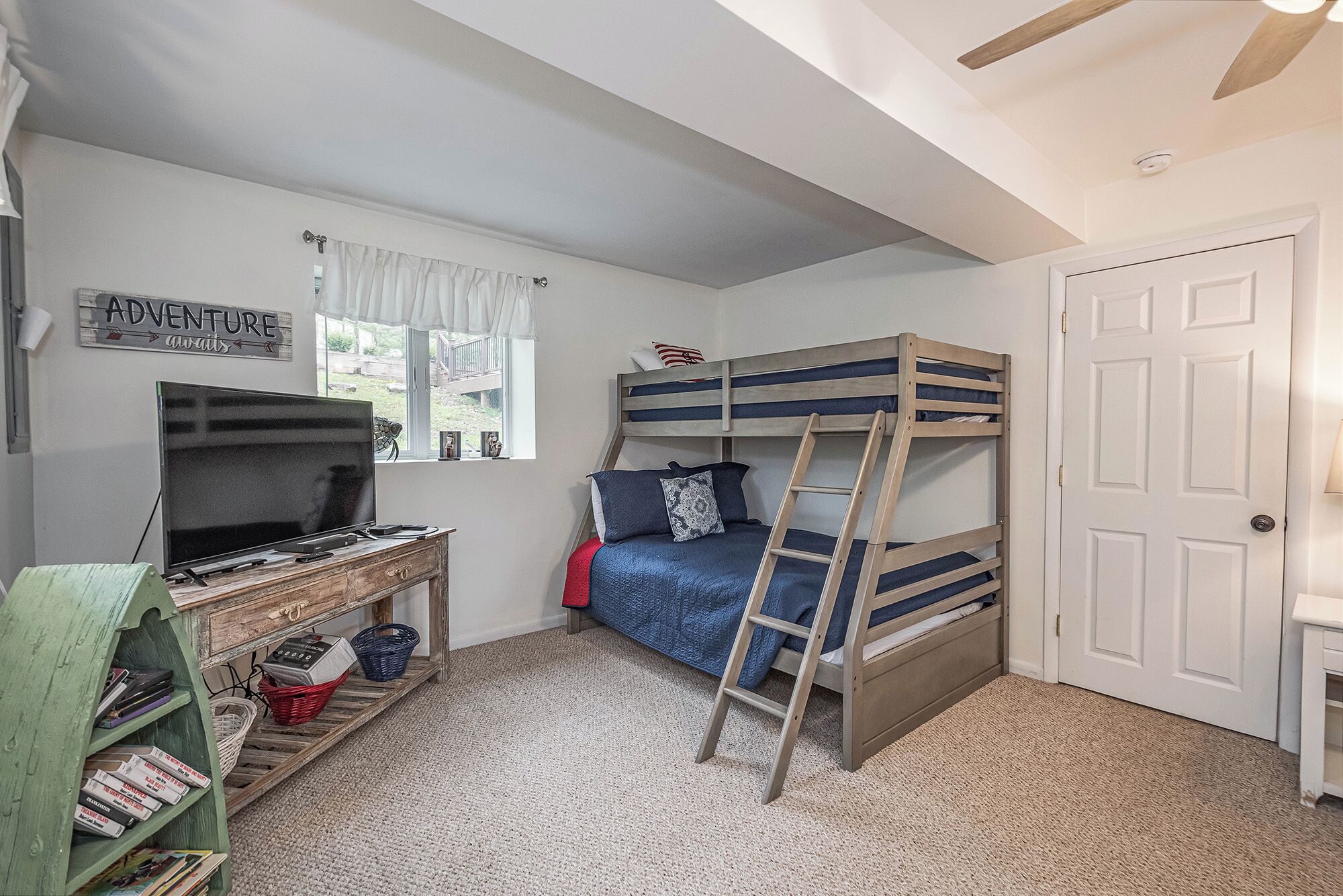 A bedroom with bunk beds, a desk with a TV, and a bookshelf.