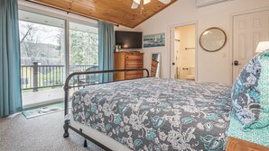 A bedroom with a bed, a dresser, a ceiling fan, a TV, and a balcony with a view of trees and a house. - Lakeside Dreamin' by Taylor Made Deep Creek (McHenry)
