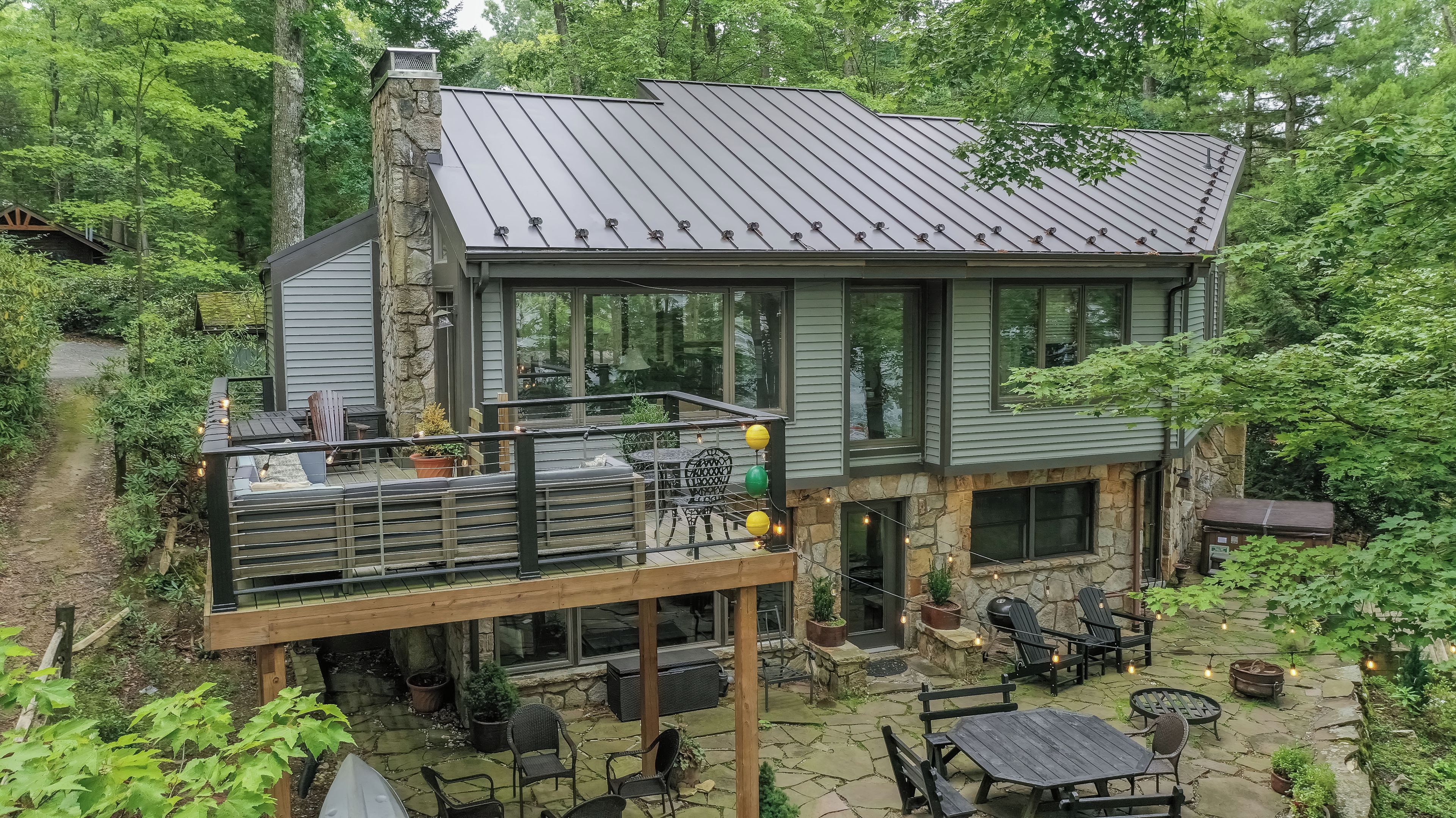 Een tweelaags huis met een stenen gevel, een balkon met buitenmeubilair en een stenen terras met zitplaatsen.