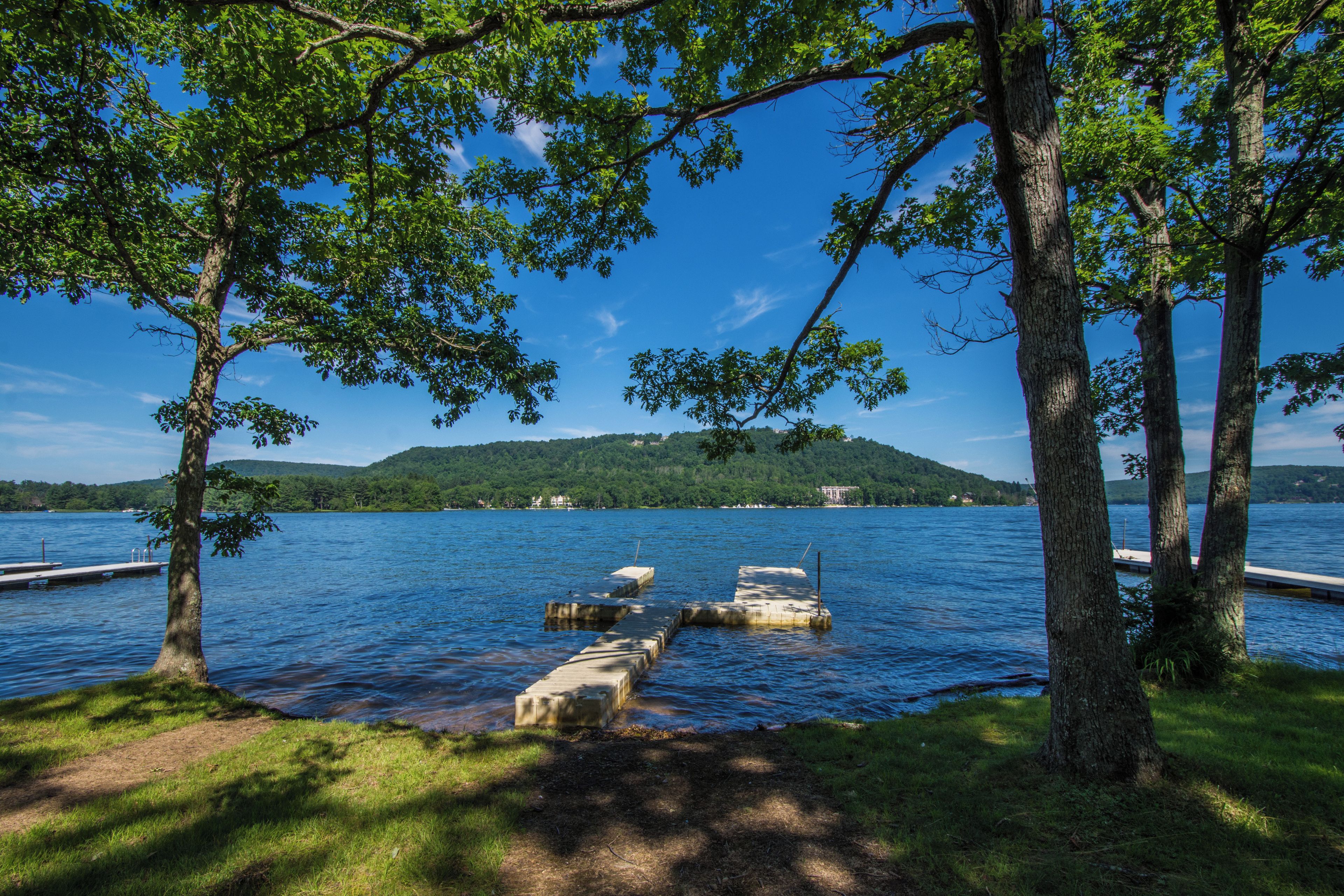 A lakeside view with a dock extending into the water, surrounded by trees and a distant hill.