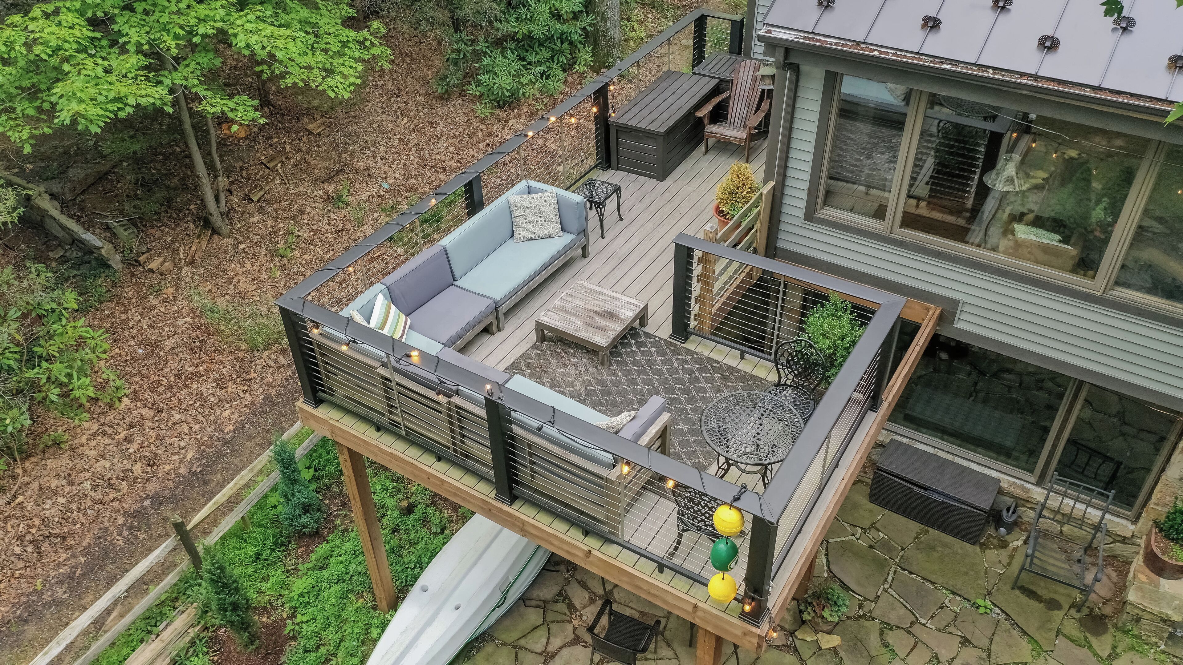 A rooftop deck with a sofa, table, and chairs, surrounded by a wooden fence and string lights.