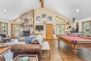 A spacious living room with a stone fireplace, a pool table, and a cozy seating area. - Lakeside Vista by Taylor Made Deep Creek (Oakland)