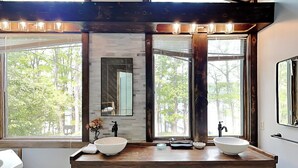 A bathroom with two sinks, wooden cabinetry, and large windows with a view of trees. - Lakeside Vista by Taylor Made Deep Creek (Oakland)