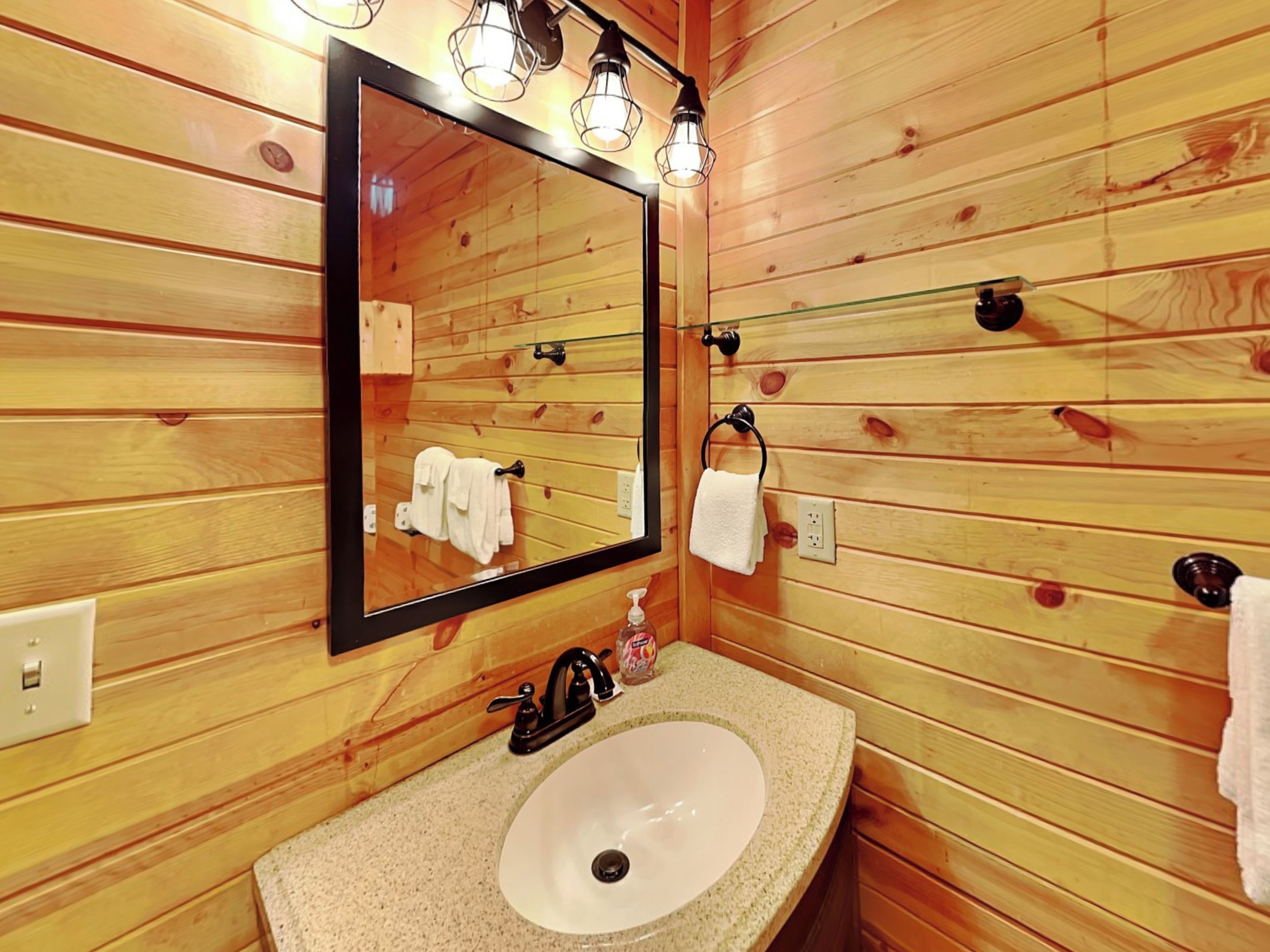 A wooden-paneled bathroom with a large mirror, a sink, and towel hooks.