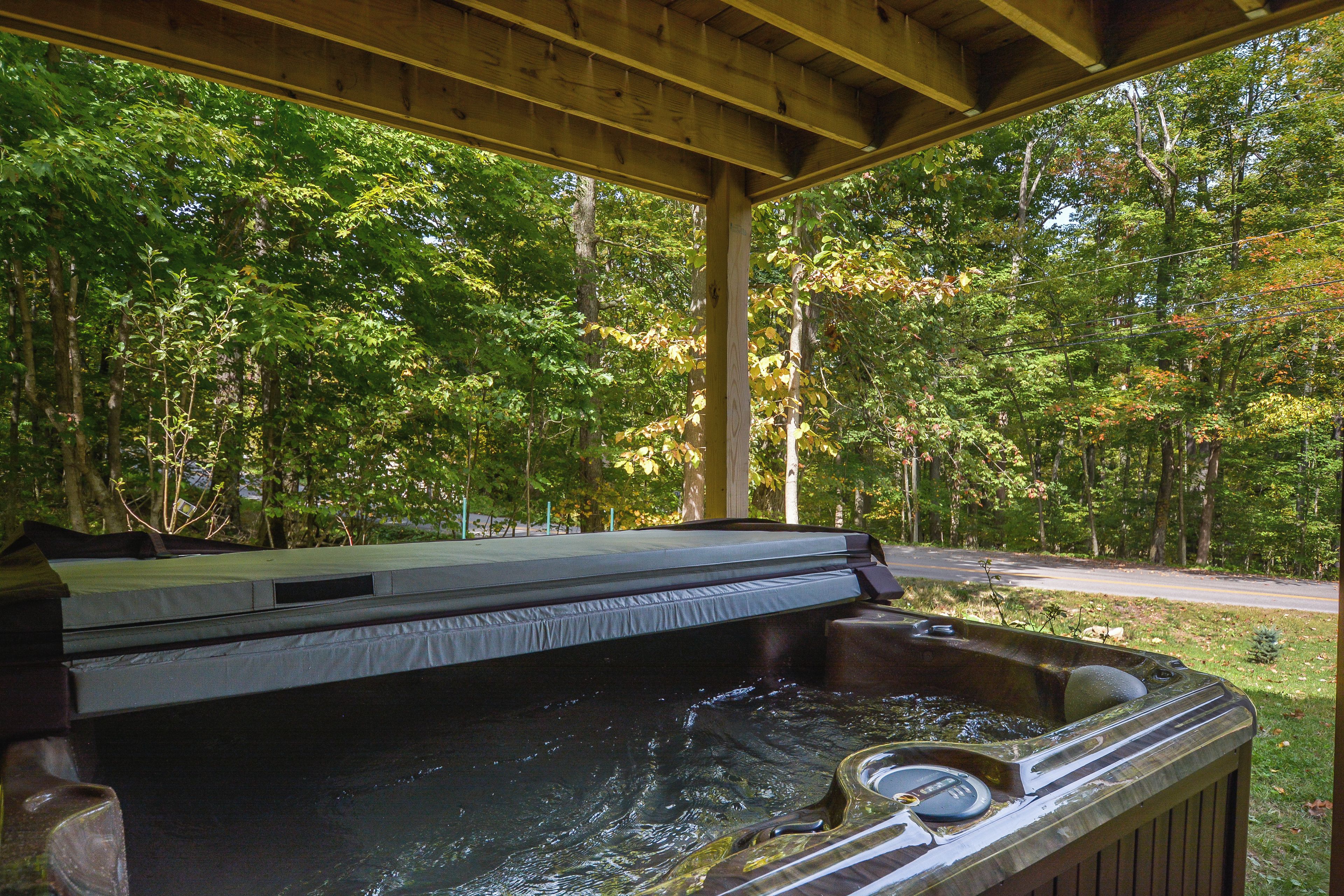 A hot tub under a wooden pavilion surrounded by trees.