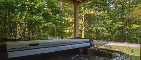 A hot tub under a wooden pavilion surrounded by trees.