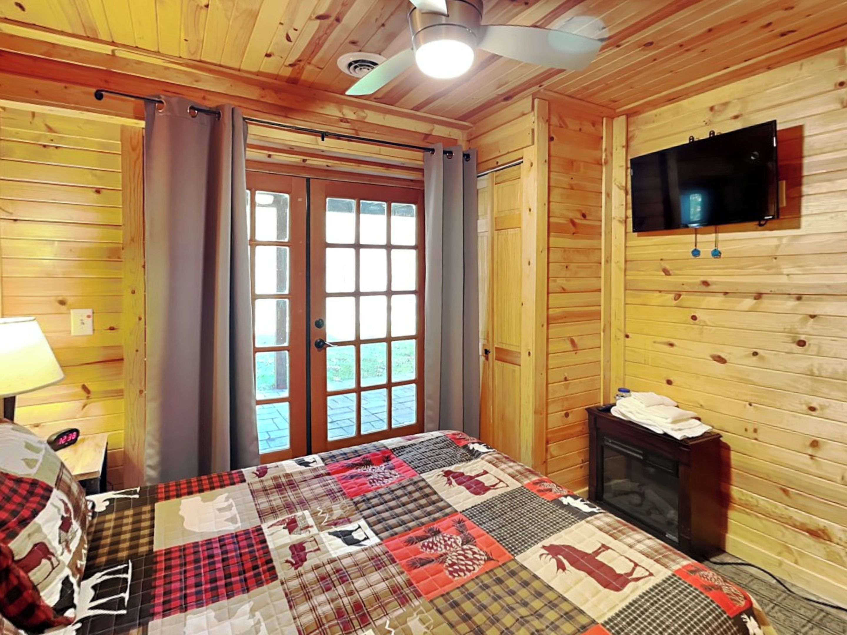 A wooden-paneled room with a bed, a television, and a window with curtains.