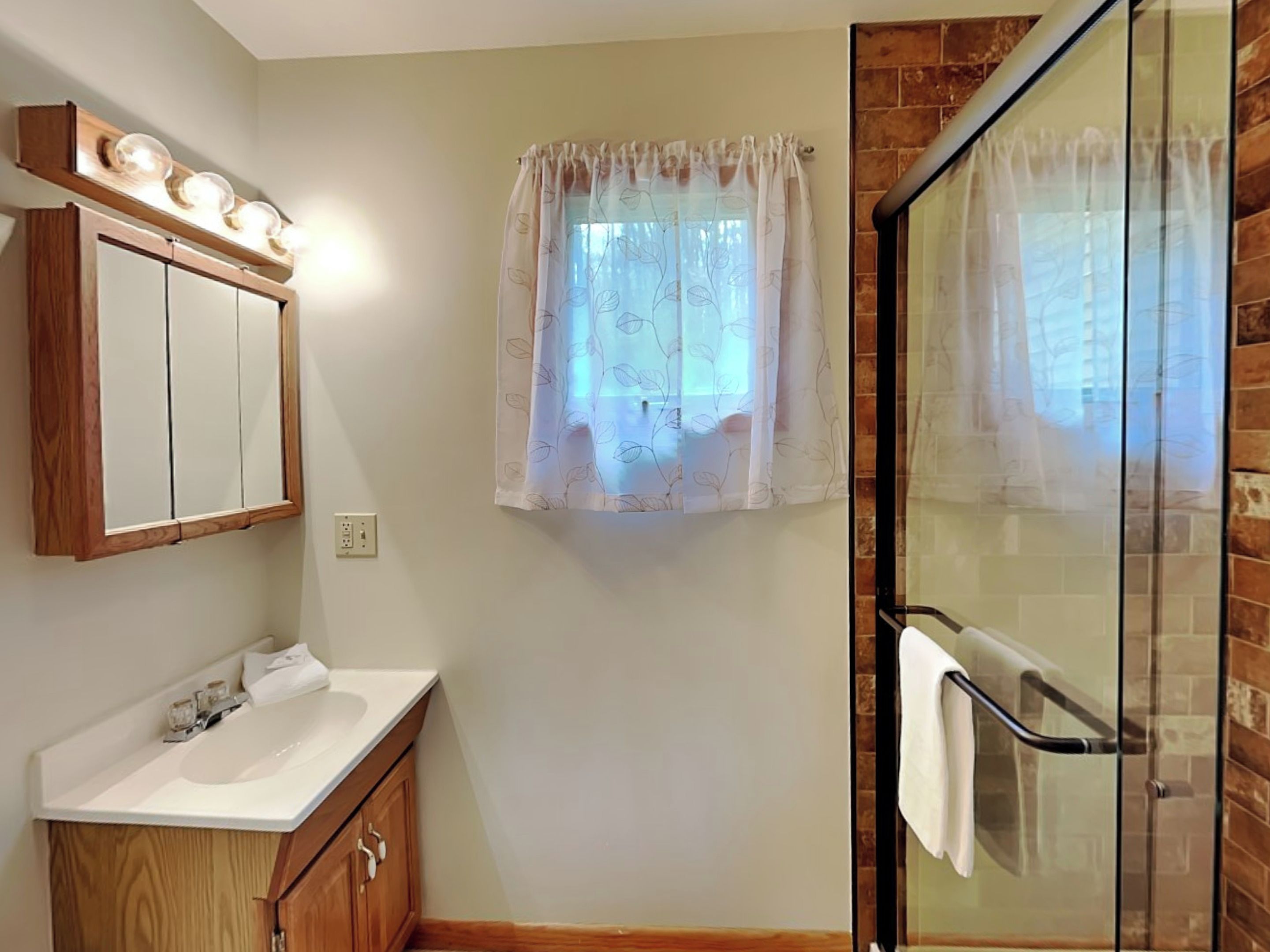 Un bagno con un mobile vanitario in legno, un lavandino bianco, uno specchio e un box doccia in vetro.