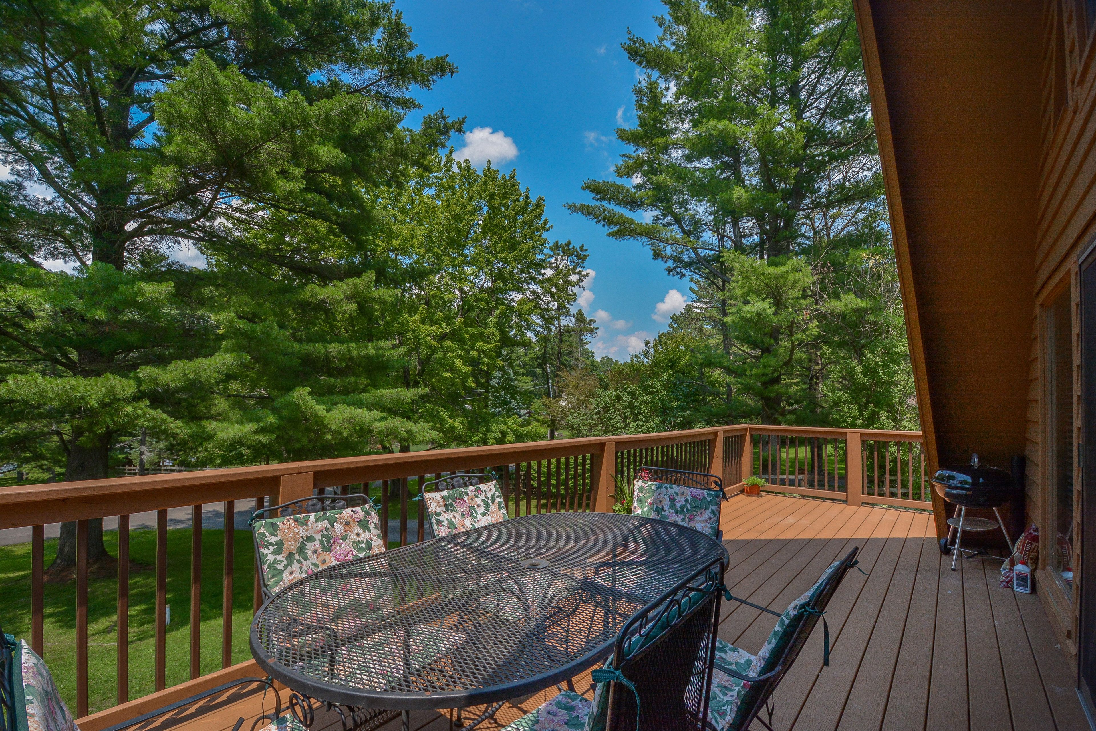 A deck with a round table and chairs, surrounded by a wooden railing, overlooking a forested area.